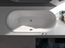 Bañera ovalada de acero esmaltado, integrada en superficie rectangular blanca, con desagüe central.